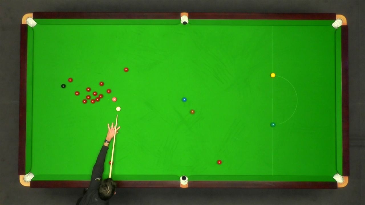 Snooker table with balls and a player's arm holding a cue, on a dark background