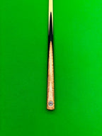 A close-up of a snooker cue shaft and butt end against a bright green felt background. The shaft is light wood with a black ferrule, and the butt cap features a circular black and red Pro Edge logo.