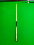 A single snooker cue laid vertically on a bright green snooker table, with a wooden handguard and a light-colored shaft.