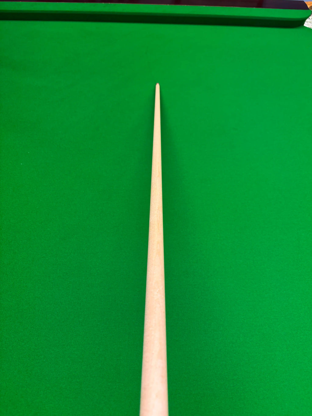 A close-up of a wooden snooker cue shaft pointing vertically upwards against a green snooker table felt background.
