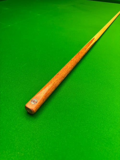 A wooden snooker cue with a natural wood finish and a small circular Pro Edge logo near the butt, resting diagonally on a bright green snooker table felt.