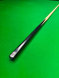 A close-up of a snooker cue shaft resting diagonally on a green felt snooker table, showing the black ferrule, white and red logo, and natural wood tip.