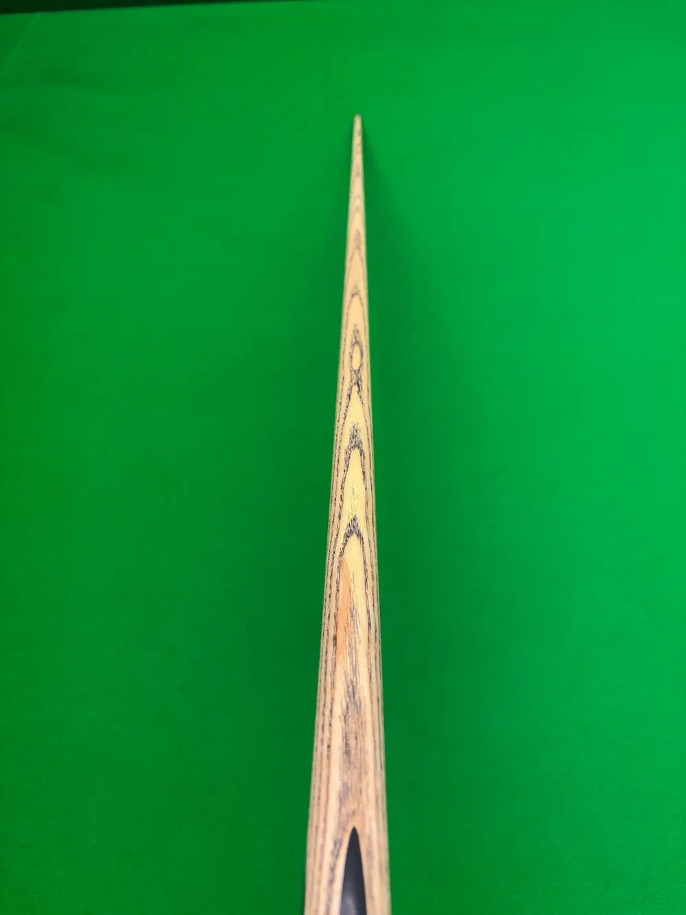 Close-up of a wooden snooker cue shaft with visible wood grain patterns, positioned vertically against a solid green background.