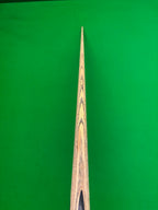 Close-up of a wooden snooker cue shaft with visible wood grain patterns, positioned vertically against a solid green background.