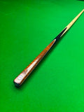 A single snooker cue resting diagonally on a green felt table cover, showing a polished wood handle with a silver-colored end cap and a black shaft.