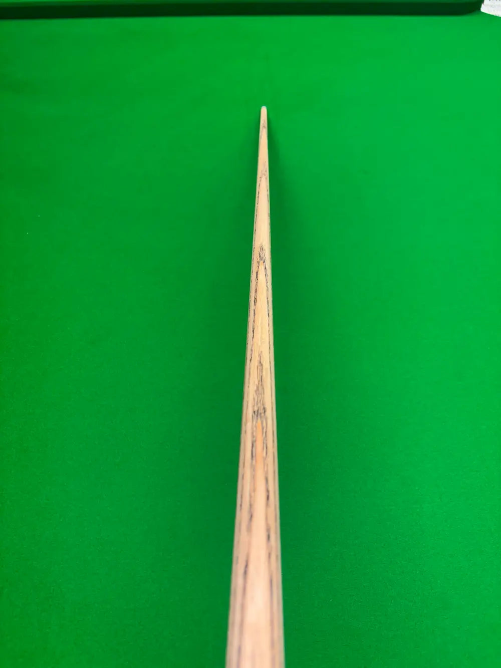 A close-up of a wooden snooker cue shaft pointing vertically down the center of a green snooker table.