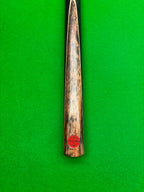 Close-up of a wooden snooker cue shaft with a red circular 'Pro Edge' brand sticker, set vertically against a bright green felt background.