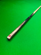 A close-up of a snooker cue shaft resting diagonally on a green snooker table, showing the wooden splice with a red Pro Edge logo