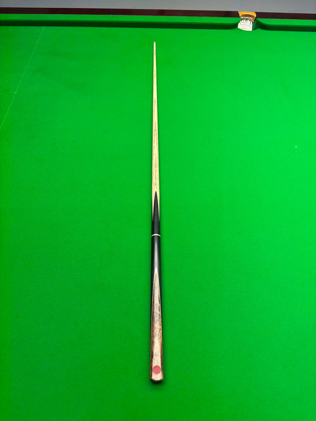 A single snooker cue laid vertically on a green snooker table, with the tip pointing toward the top edge of the frame.