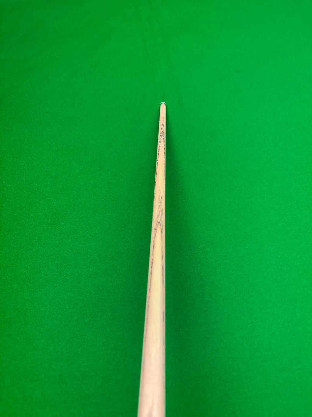 A close-up of a wooden snooker cue shaft standing vertically against a bright green felt background.