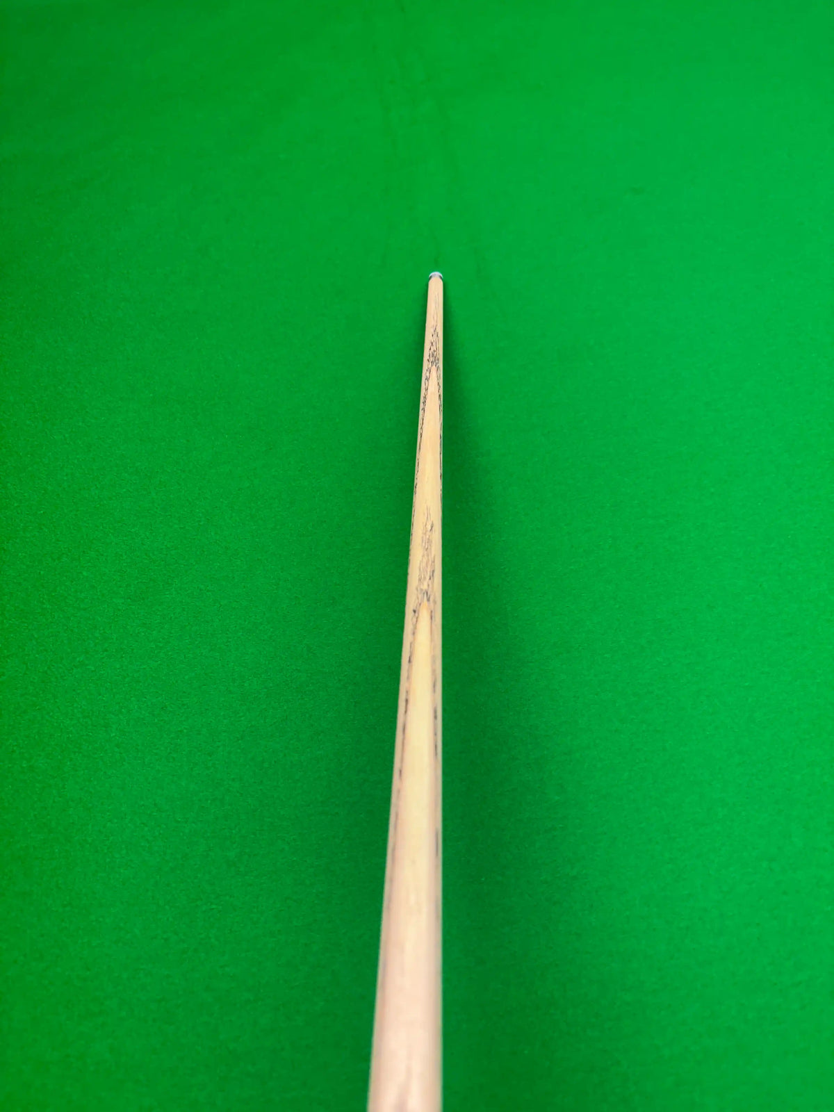 A close-up of a wooden snooker cue shaft standing vertically against a bright green felt background.