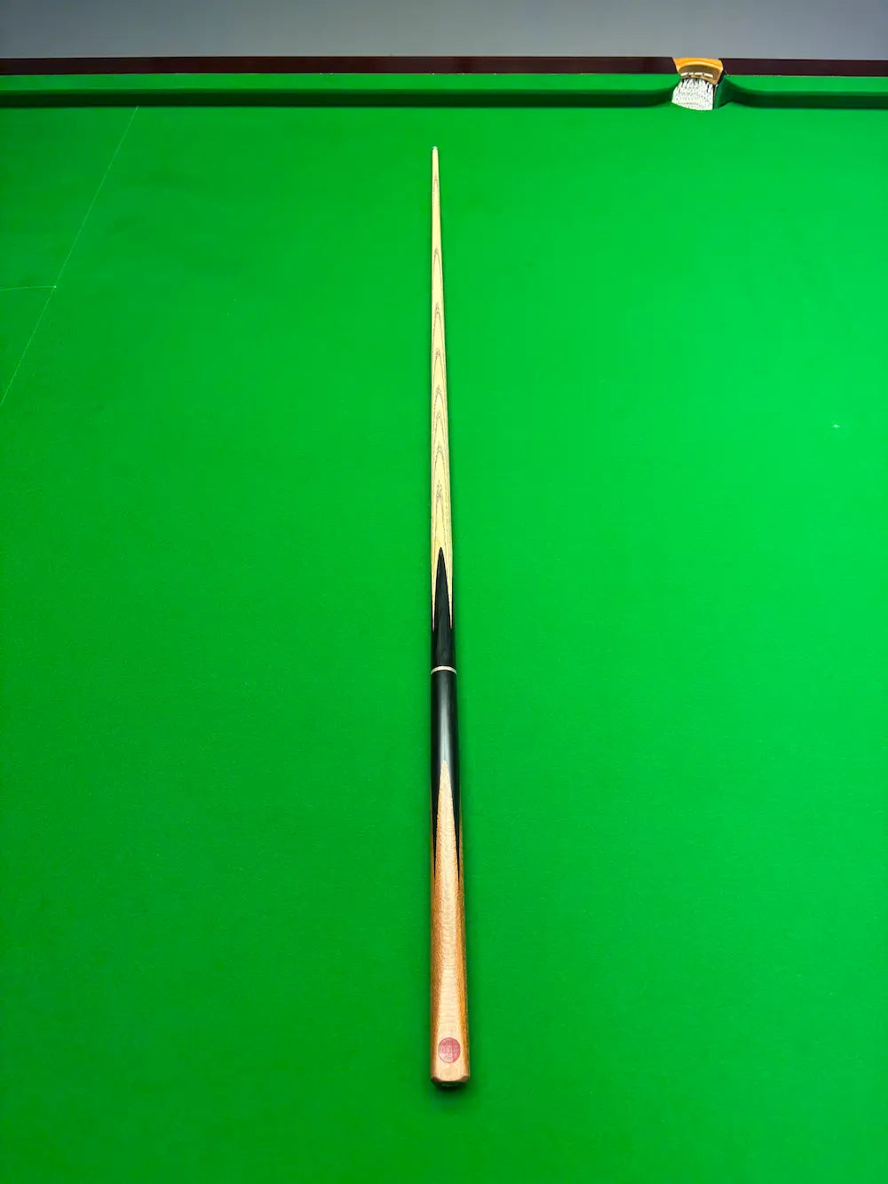 A single snooker cue shown vertically on a green snooker table, with the tip pointing toward the top edge of the frame.