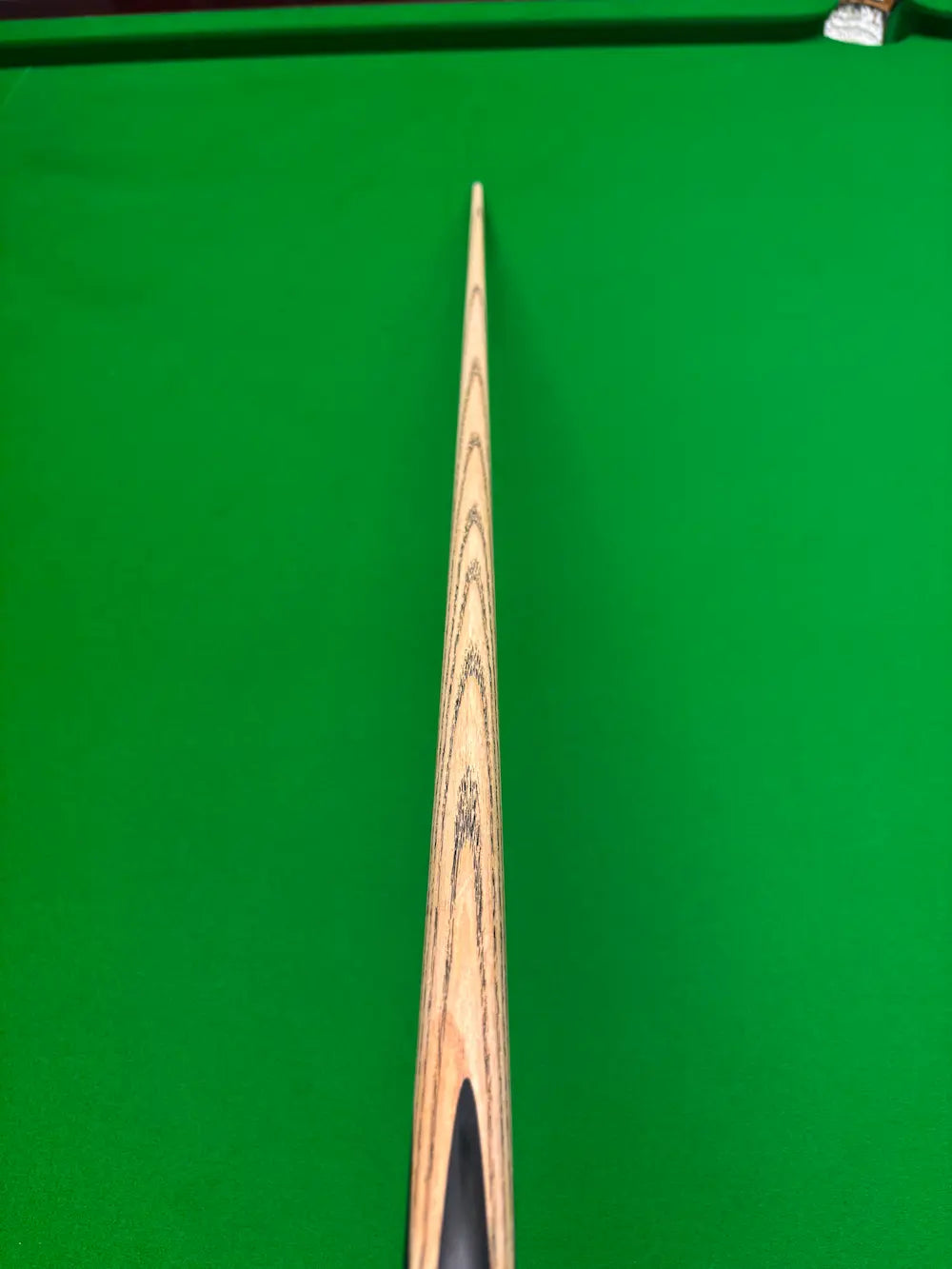 A close-up, top-down view of a wooden snooker cue shaft resting vertically on a green snooker table.