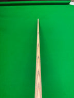 A close-up of a wooden snooker cue shaft pointing down the center of a green snooker table.