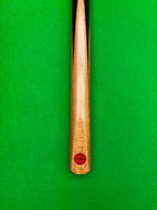 Close-up of a wooden snooker cue shaft with a red circular 'Pro Edge' brand badge, laying on a snooker table