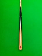 A close-up of a snooker cue shaft with a black and light wood striped finish and a red circular logo near the butt, set against a solid green felt background.