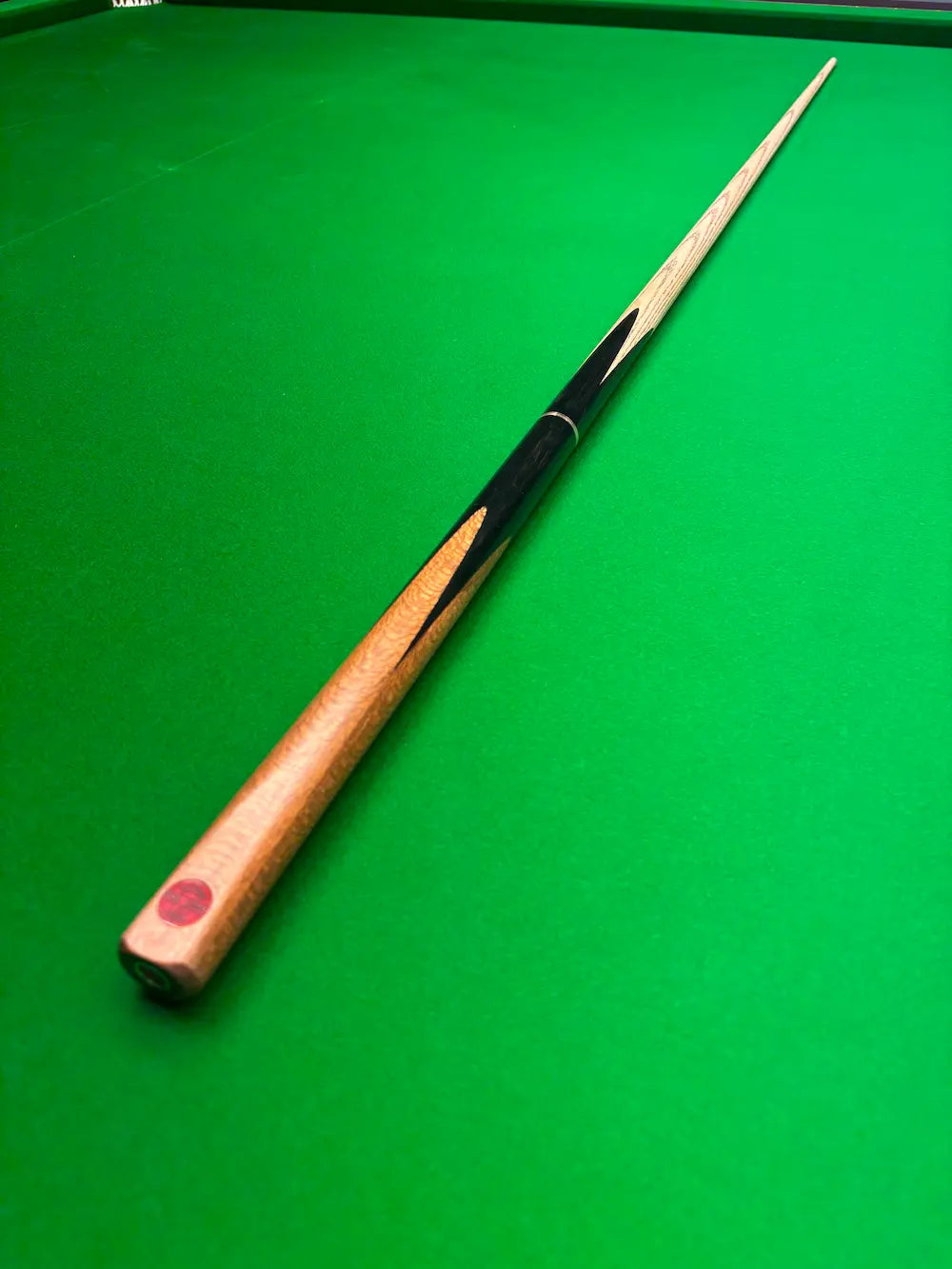 A wooden snooker cue with a black and dark brown striped shaft, resting diagonally on a green snooker table.