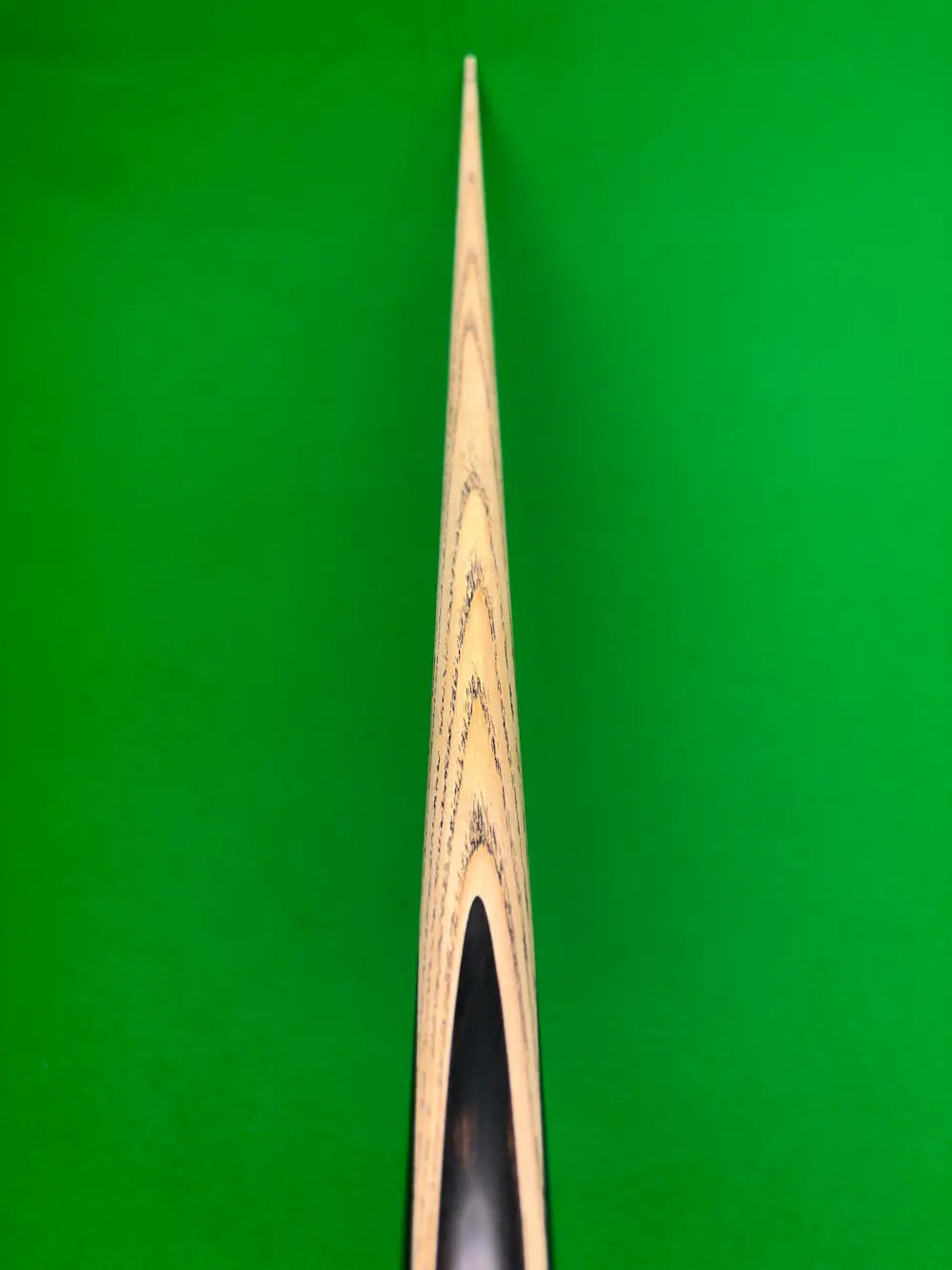Close-up of a wooden snooker cue against a bright green felt background.