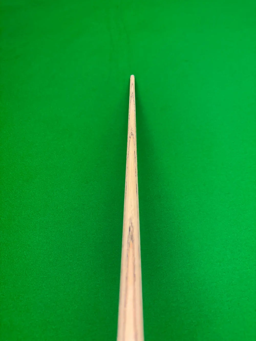 Close-up of a wooden snooker cue shaft pointing upward toward a bright green snooker table felt surface.