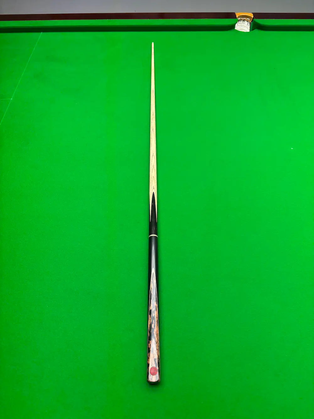 A single snooker cue laid vertically on a green snooker table, with the tip pointing upward toward the top rail.