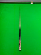 A single snooker cue laid vertically on a green snooker table, with the tip pointing upward toward the top rail.