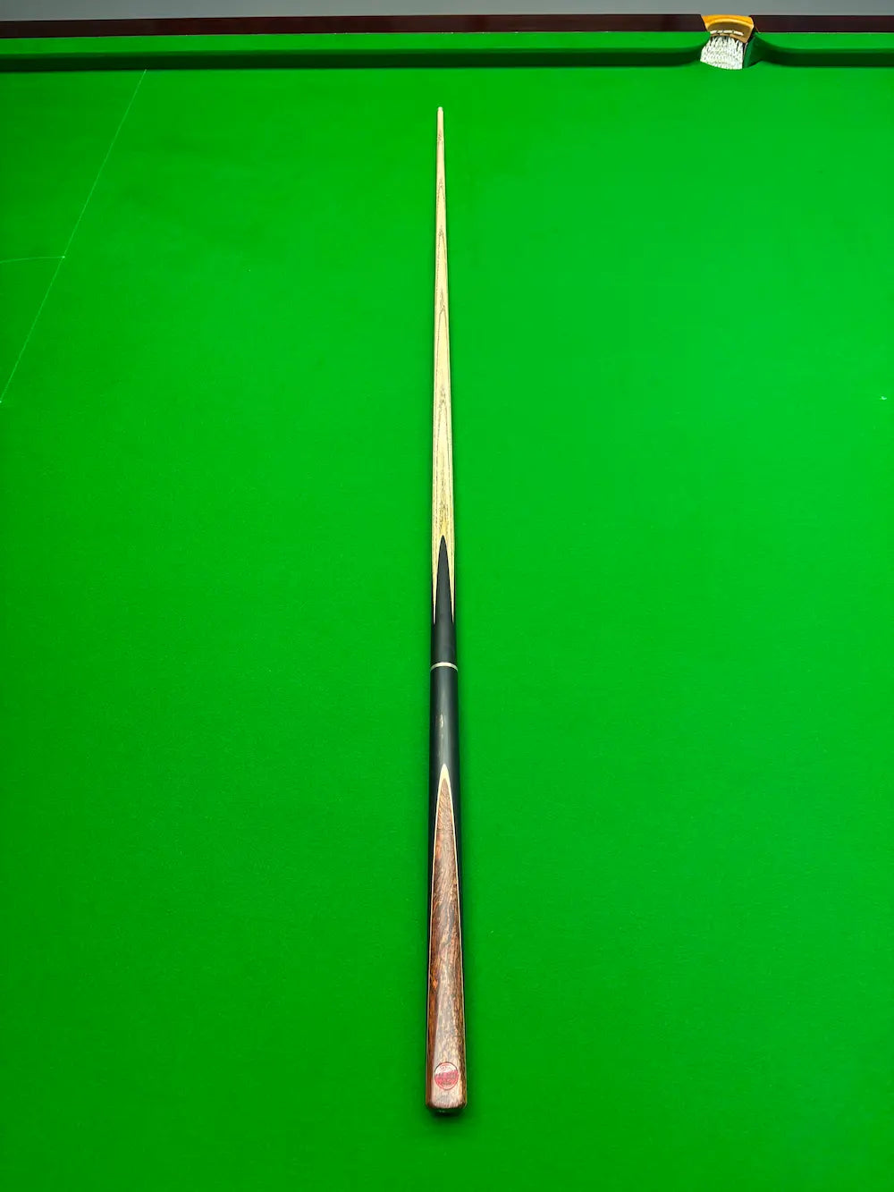 A single snooker cue laid vertically on a bright green snooker table, with the tip pointing upward toward the top edge of the frame.