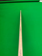 A close-up, top-down view of a wooden snooker cue shaft positioned vertically against a bright green snooker table felt background.