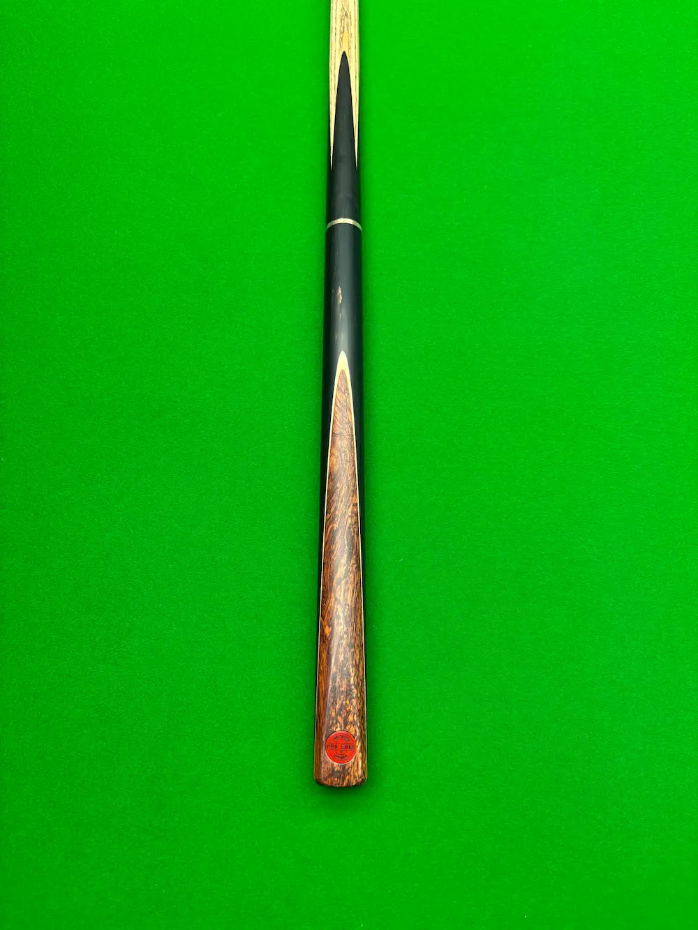 A close-up of a wooden snooker cue shaft resting vertically on a bright green felt surface.