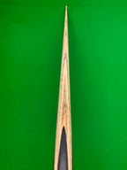 Close-up of a wooden snooker cue shaft with a black ferrule, positioned vertically against a bright green snooker table felt background.