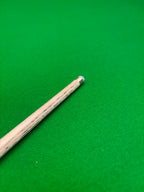 A close-up of a wooden snooker cue shaft with a silver-colored ferrule, resting diagonally on a vibrant green felt surface.