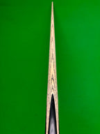 Close-up of a wooden snooker cue shaft with black grain patterns, centered vertically against a bright green background.