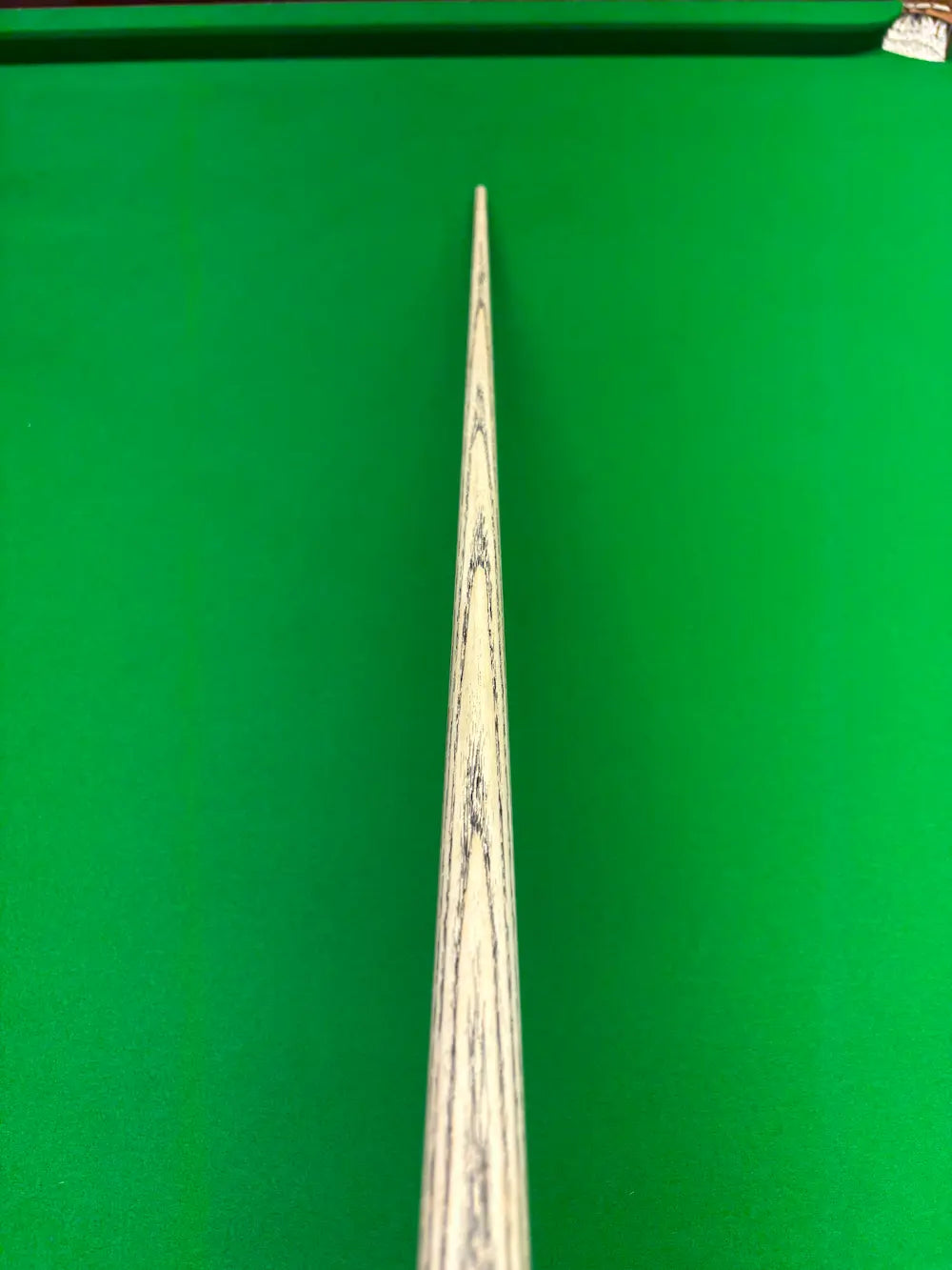 Close-up of a wooden snooker cue shaft with dark grain lines, positioned vertically against a bright green snooker table felt background.