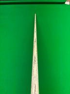 Close-up of a wooden snooker cue shaft with dark grain lines, positioned vertically against a bright green snooker table felt background.