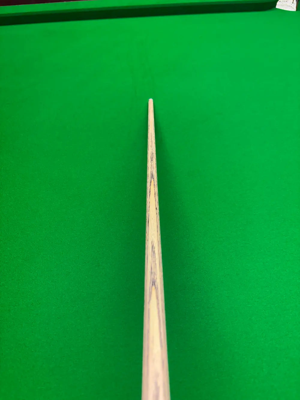 A close-up view of a wooden snooker cue pointing down the cushion of a green snooker table.