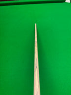 A close-up view of a wooden snooker cue pointing down the cushion of a green snooker table.