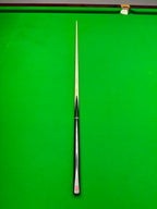 A single snooker cue with a silver ferrule and black grip, laid vertically on a green snooker table.