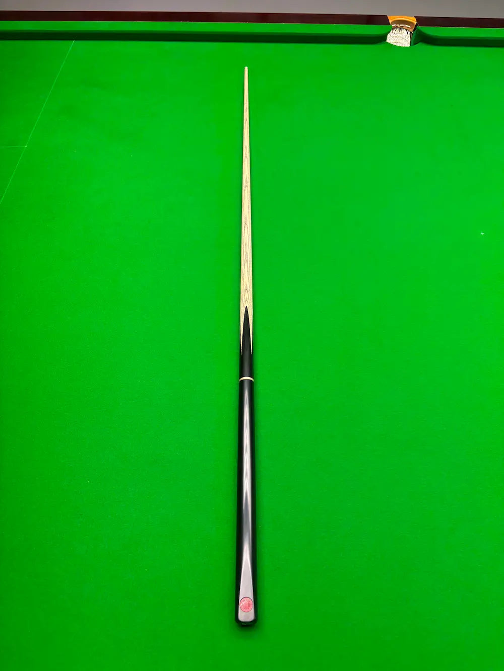 A single snooker cue with a silver ferrule and black grip, laid vertically on a green snooker table.
