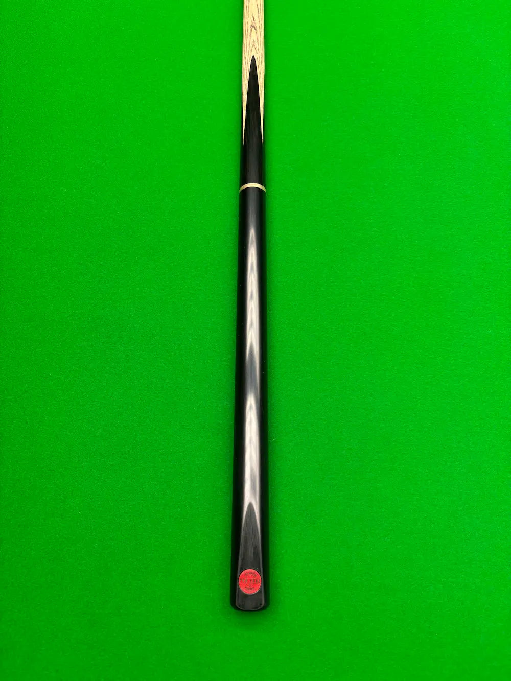 A close-up of a snooker cue shaft with a black handle and a red Pro Edge logo near the butt, set against a bright green snooker table felt background.