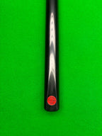 Close-up of a black snooker cue shaft with a red circular Pro Edge' brand sticker, positioned vertically against a bright green snooker felt background.