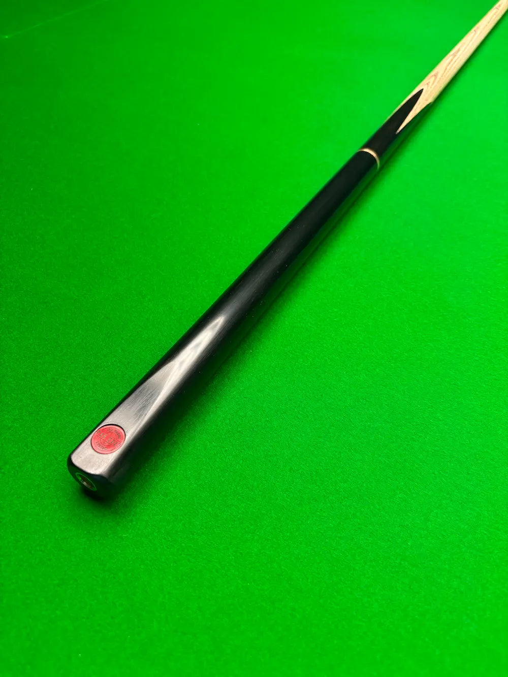 A close-up of a black snooker cue shaft with a red Pro Edge logo near the butt, resting diagonally on a green felt table surface.
