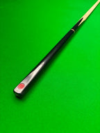 A close-up of a black snooker cue shaft with a red Pro Edge logo near the butt, resting diagonally on a green felt table surface.