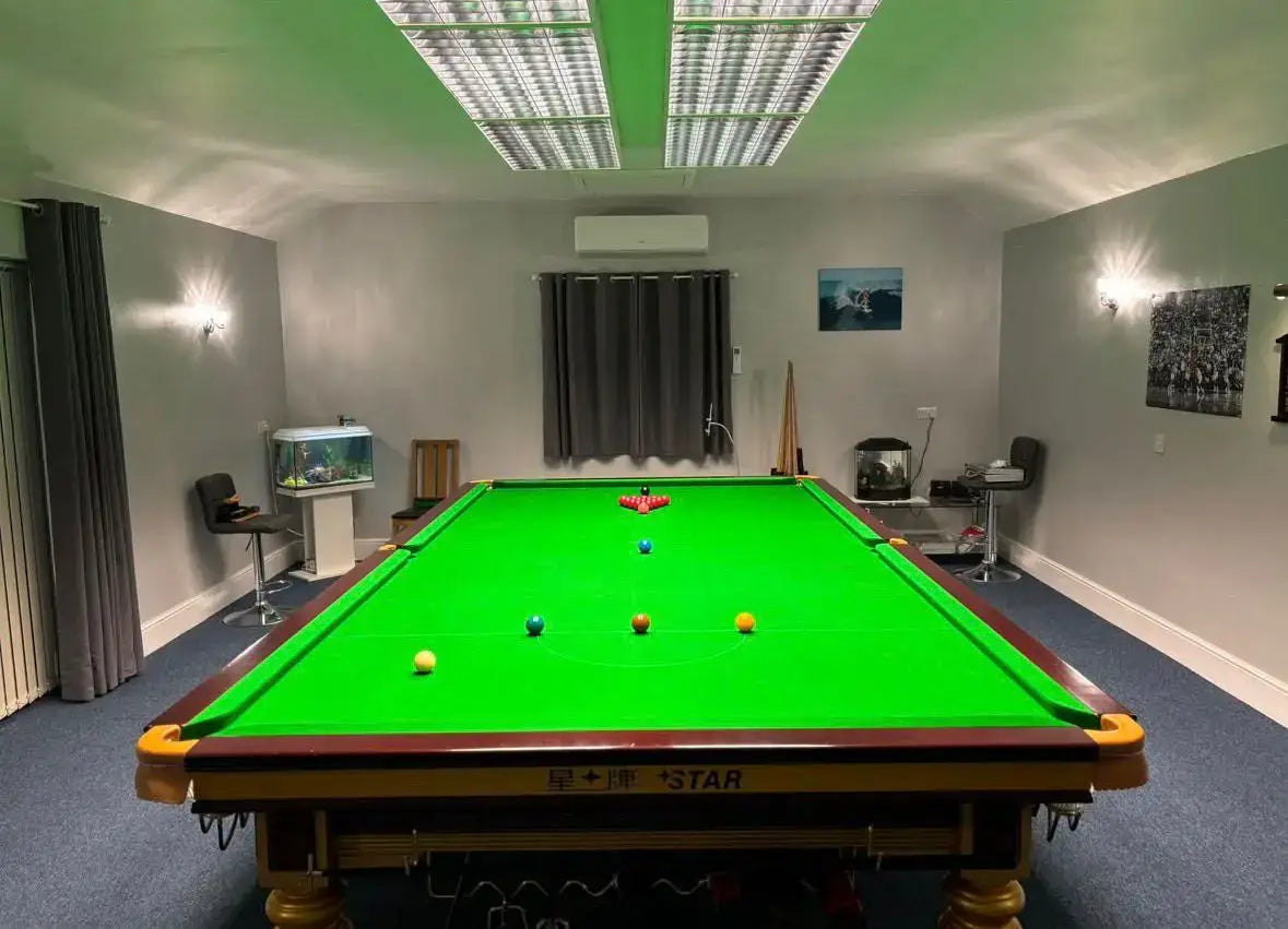 Snooker table with green cloth and red ball in a room with gray walls and carpet.