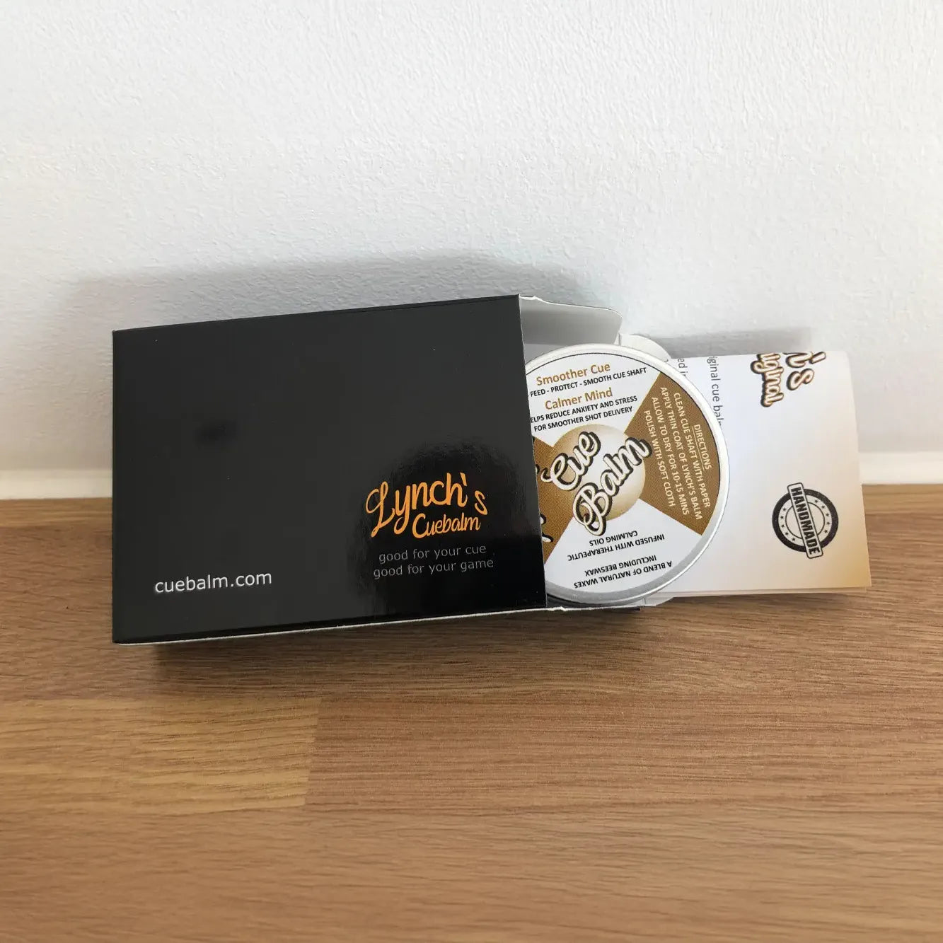 Cue balm packaging with black box and white container on a wooden surface