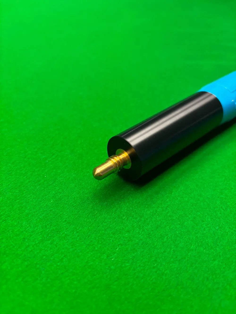Close-up of a snooker cue extension with a black and blue grip, featuring a brass ball end, resting on a green felt table surface.